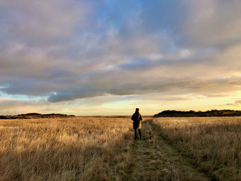 Rear view of woman standing on land against sky during sunset