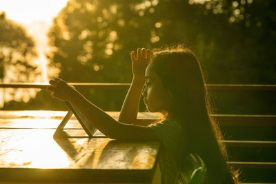 Little girl using tablet pad while sitting in outdoor during sunrise.