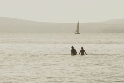 Men sailing on sailboat in sea against sky