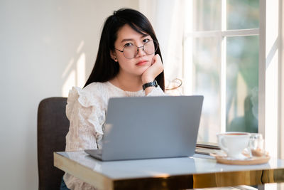 Portrait of young woman using phone while sitting on table