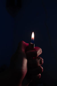 Close-up of hand holding lit candle in the dark