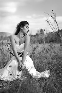 Young woman sitting on field against sky