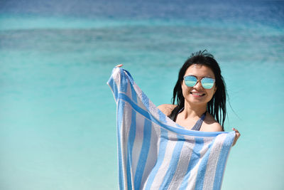 Portrait of young woman at sea while holding towel against sky
