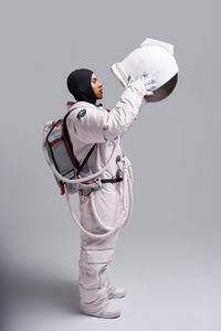 Side view of astronaut in spacesuit taking off protective helmet with visor in studio against white background