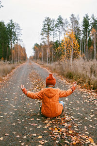 Girl sits in yoga pose on road in fall forest. deep in thoughts, daydreaming, mental health, autumn
