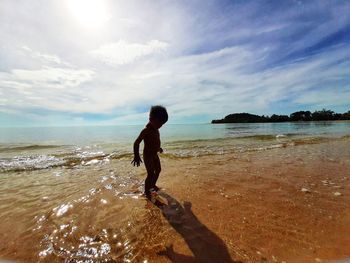 Silhouette boy standing at beach against sky