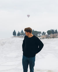 Rear view of young man standing on beach during winter