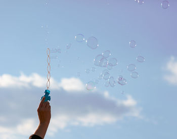 Low angle view of hand holding bubbles against sky