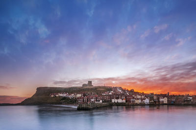 Scenic view of sea by buildings against sky at sunset