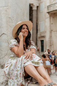 Woman in a hat talking on a cell phone while sitting by a column of ancient building