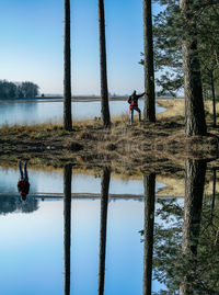 Reflection of young woman standing on lake against sky