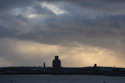 Sea by buildings against sky during sunset