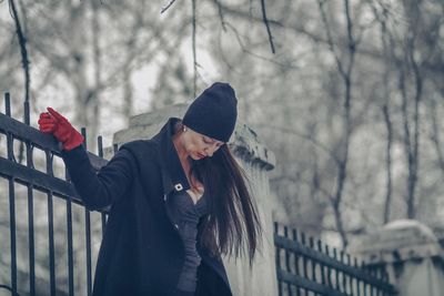 Woman standing against fence during winter