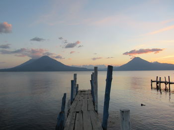 Wooden posts in sea against sky during sunset