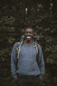 Portrait of smiling man with hands in pockets in forest