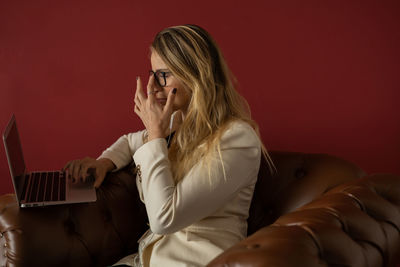 Woman working at home with laptop classic brown arm chair. red  wall home office. gray notebook 