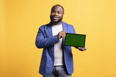 Portrait of man using digital tablet while standing against yellow background