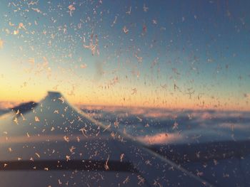 Close-up of raindrops on window against sky during sunset