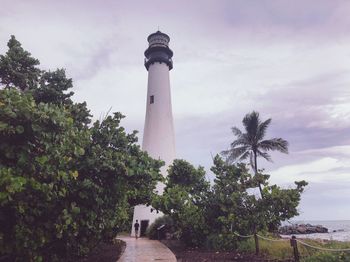 Lighthouse amidst trees and buildings against sky