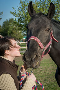 Smiling woman standing with horse on grassy field at farm