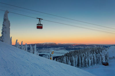 Overhead cable car on snow covered landscape against sky during sunset