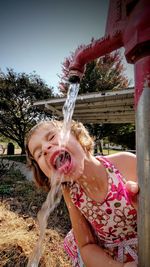 Girl drinking water from faucet on field