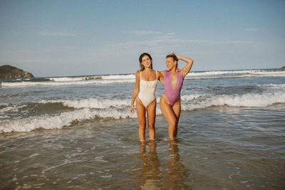 Full length of young woman standing in sea against sky