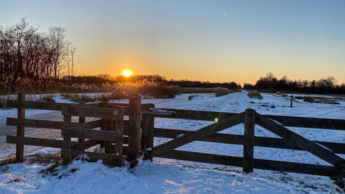 Snow covered field against sky during sunset