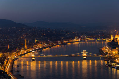 Illuminated bridge over river in city at night