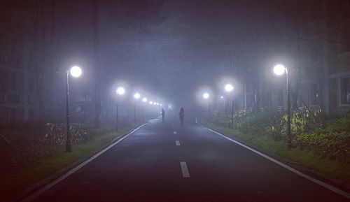 Rear view of man walking on illuminated road at night