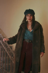 Portrait of woman in hat standing against wall