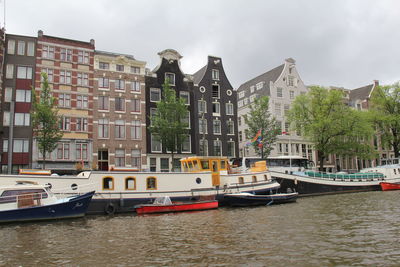 Sailboats moored on river by buildings in city against sky