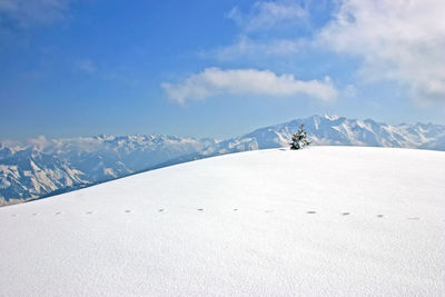 Snow covered landscape by mountains against blue sky