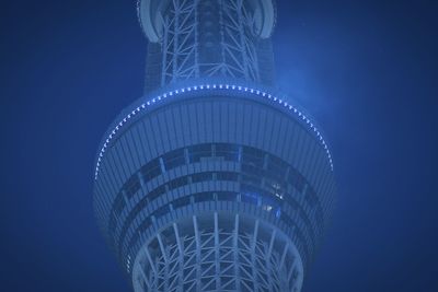 Low angle view of illuminated skyscraper against blue sky