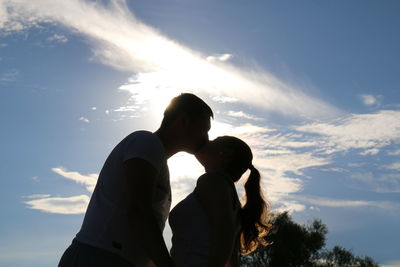 Low angle view of couple kissing on the mouth while standing against sky at sunset