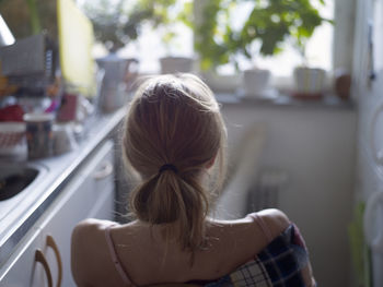 Young woman sitting in kitchen, rear view