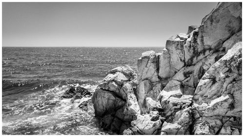 Rock formation by sea against clear sky