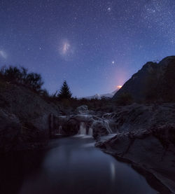 Scenic view of waterfall and mountains against sky at night