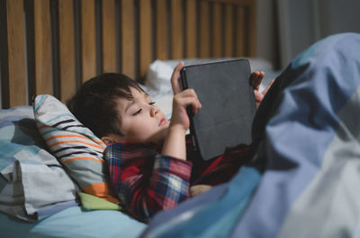 Cute boy using digital tablet while lying on bed at home