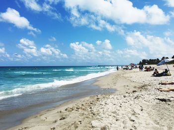 Scenic view of people on beach against cloudy sky