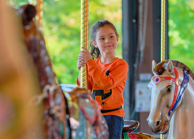 Pretty girl in a halloween themed shirt is riding a carousel at the carnival