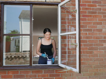 Smiling young woman painting window frame