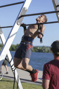 Disabled shirtless athlete practicing chin-ups against sky at park