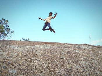 Low angle view of man jumping on land against clear sky