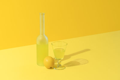 Bottle and glass of lemon liqueur limoncello on a yellow background. italian drink made with lemons
