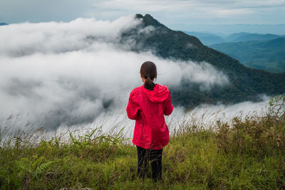 Rear view of woman standing on field against cloudy sky