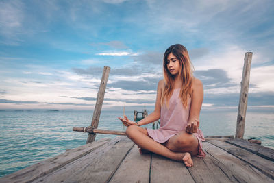 Young woman sitting on wood against sky