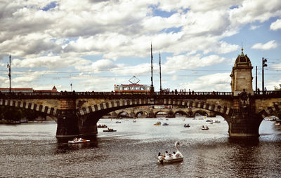 People in boat on river by bridge against cloudy sky