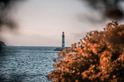 Lighthouse amidst sea and buildings against sky