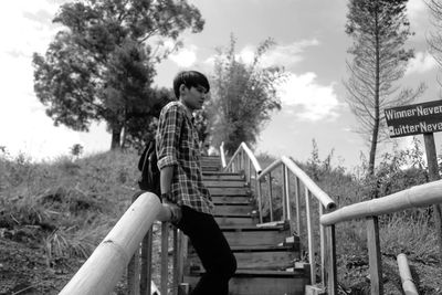 Low angle view of boy standing by railing on steps against sky